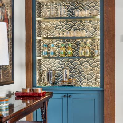 A stylish bar cabinet with glassware and decorative bottles, illuminated against a patterned backdrop.