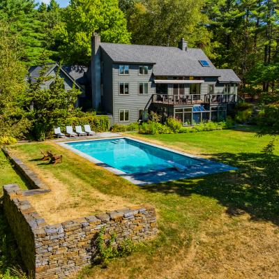 A modern house with a pool surrounded by greenery and deck chairs.