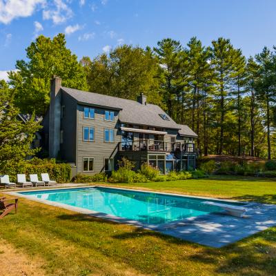 Elegant house with a pool surrounded by greenery and tall trees under a clear blue sky.