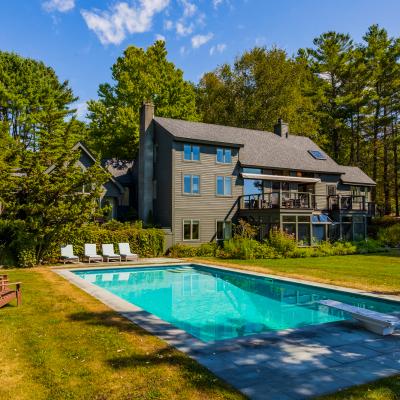 Modern house with a pool, surrounded by trees and lawn chairs in a serene outdoor setting.