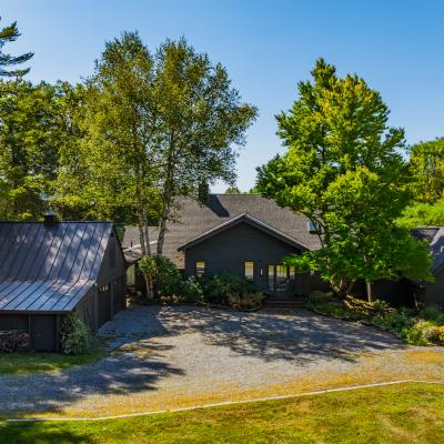 A modern house surrounded by trees and a gravel driveway under a clear blue sky.