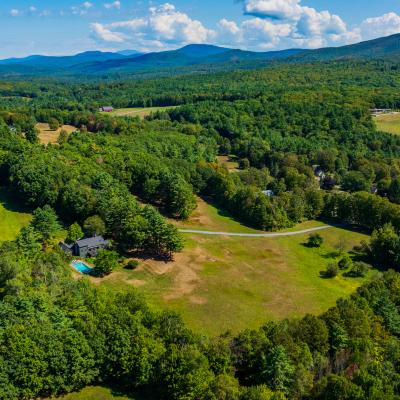 Aerial view of lush green landscape with a house, pool, and hills in the background.