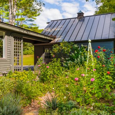 Charming house with a metal roof surrounded by lush gardens and colorful flowers.