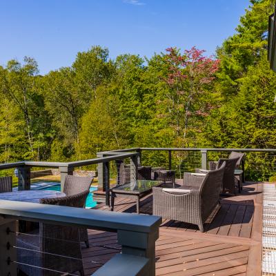 Sunny deck with brown wicker furniture overlooking lush green trees.