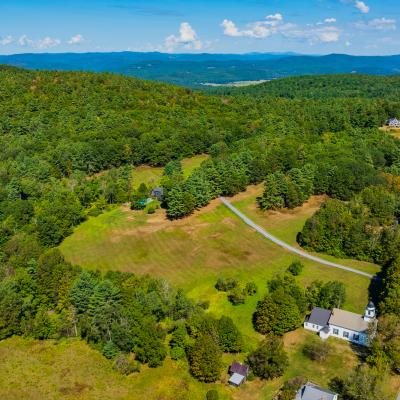Aerial view of lush green hills, fields, and a few houses under a clear blue sky.