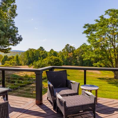 View from a deck with wicker chairs overlooking a lush green landscape and trees.