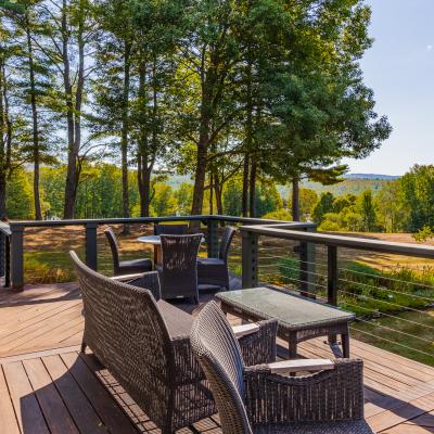 A scenic deck with wicker furniture overlooks a lush green landscape and trees.