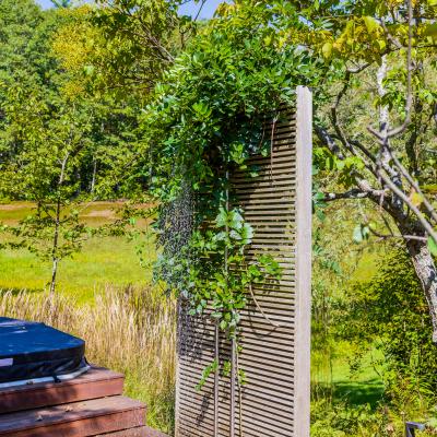 Outdoor shower with wood paneling, surrounded by greenery and a sunny landscape.