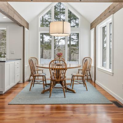 Cozy dining area with wooden chairs, round table, and bright windows overlooking trees.