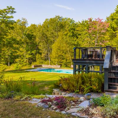 A serene backyard with a pool, deck, and lush green trees.