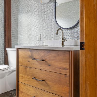 Stylish bathroom featuring a wooden vanity, round mirror, and geometric wallpaper.