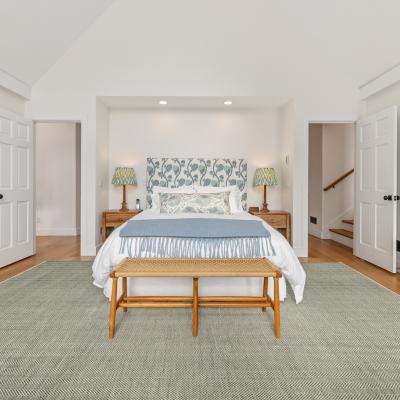 Bright bedroom featuring a bed with patterned headboard, nightstands, and a woven bench.