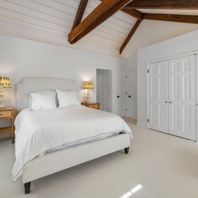 Bright bedroom with wooden beams, a bed, nightstands, and a cozy armchair.