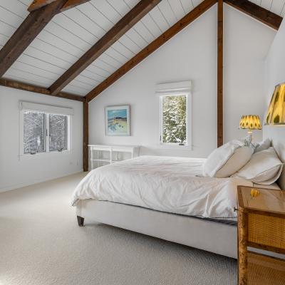 Bright bedroom with vaulted ceiling, cozy bed, and large windows showing snowy scenery.