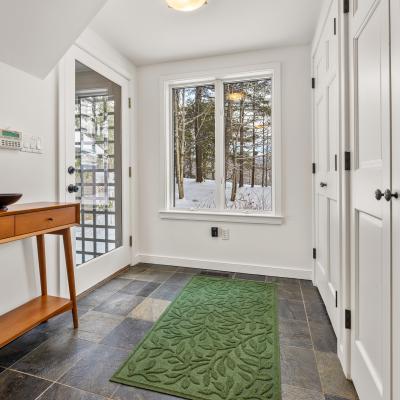 Modern entryway with a wooden table, green rug, and snowy outdoor view.