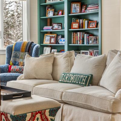 Cozy living room with a sofa, patterned ottoman, and a bookshelf filled with photos and books.