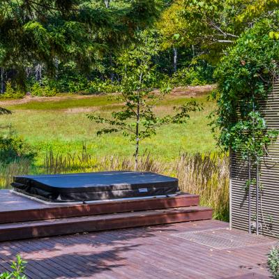 Hot tub on a wooden deck surrounded by lush greenery and a serene landscape.