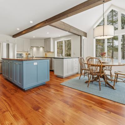 Bright, modern kitchen with an island, dining area, and large windows overlooking nature.