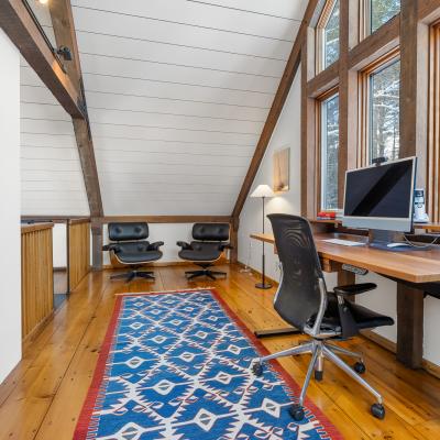 Cozy workspace with large windows, wood beams, modern desk, and two chairs.