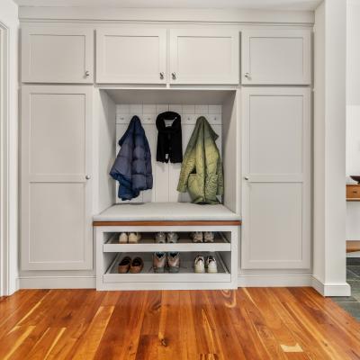Entryway with a bench, hanging coats, and shoe storage under a light gray cabinet.
