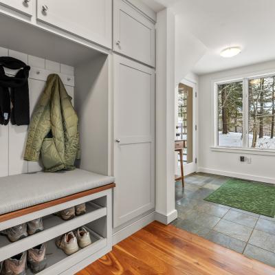 Mudroom with hooks, seating, shoes, and a view of snow-covered trees outside.