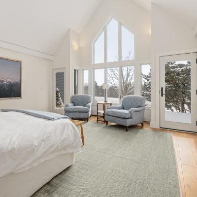 Bright, cozy bedroom with a bed, two blue chairs, a large window, and mountain artwork.