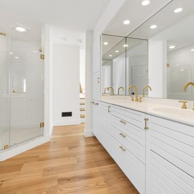 Modern bathroom featuring a glass shower, double vanity, and gold fixtures on wooden flooring.