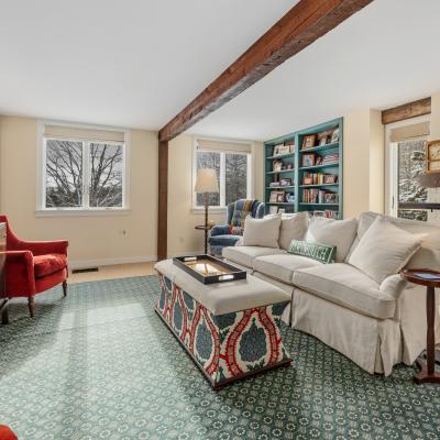 Cozy living room with a couch, bookshelves, and large windows, featuring wooden beams.