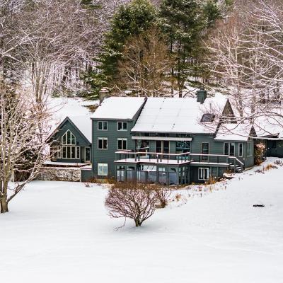 A large, snow-covered house surrounded by trees in a winter landscape.