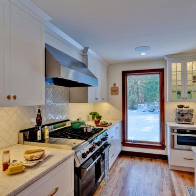 Modern kitchen with white cabinets, stove, and window overlooking snowy outdoors.