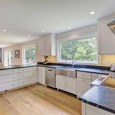 Modern kitchen with white cabinets, black countertops, and large windows overlooking greenery.