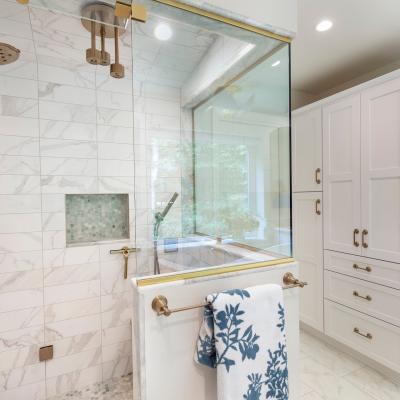 Modern bathroom with glass shower, marble tiles, and white cabinetry.