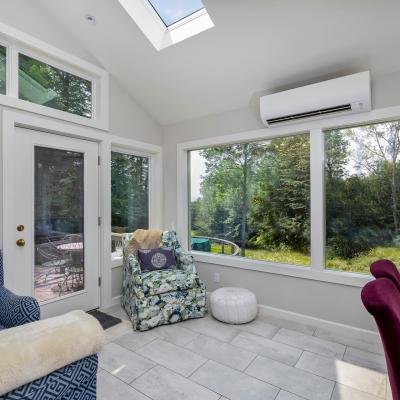 Bright sunroom with seating, large windows, and views of greenery outside.