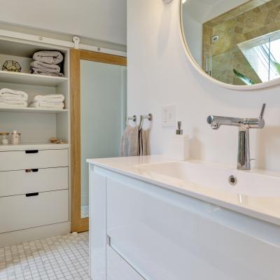 Modern bathroom with white vanity, round mirror, and neatly organized storage.