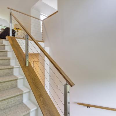 Modern staircase with wooden railing and sleek cable design, leading to a bright space.