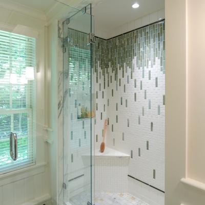 Modern shower with glass door, tiled walls, and a built-in bench. Bright natural light.