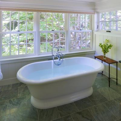 Bright bathroom with a freestanding tub, large windows, and natural greenery outside.