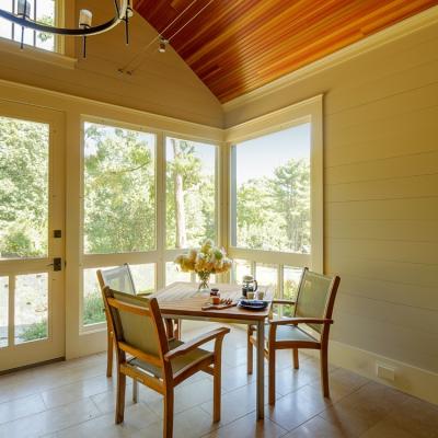 Bright sunroom with two chairs, a table set for tea, and large windows overlooking greenery.