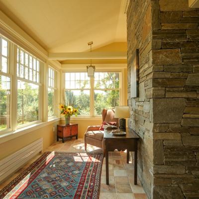Bright sunroom featuring a stone wall, armchair, and colorful rug with flowers.