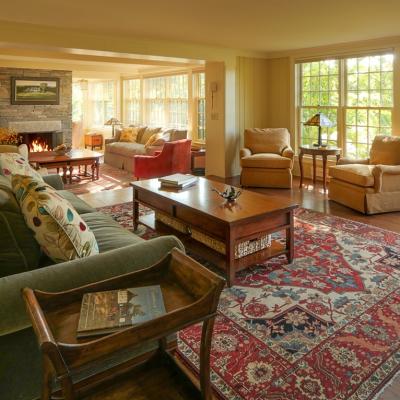 Cozy living room with a fireplace, sofas, and large windows revealing greenery outside.