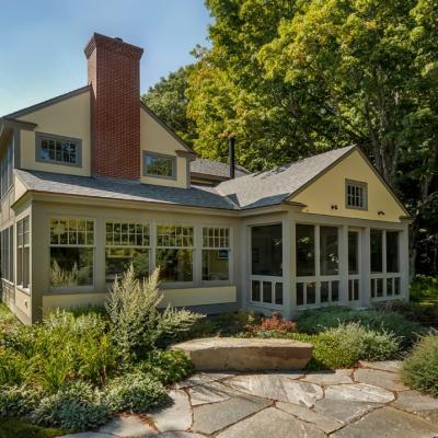 Charming house with a screened porch, surrounded by greenery and landscaped stones.