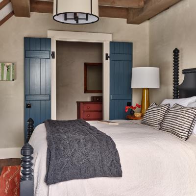 Cozy bedroom with a quilted bedspread, dark blanket, and blue shutters.