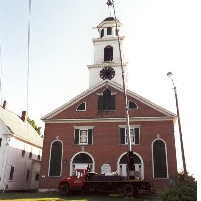 A red truck with a lift near a brick building's clock tower for maintenance.
