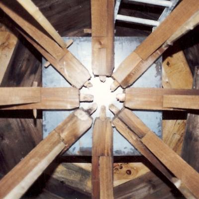View from below of wooden beams converging at a central metal plate.