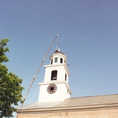 Clock tower under blue sky, with a crane at the top for maintenance work.
