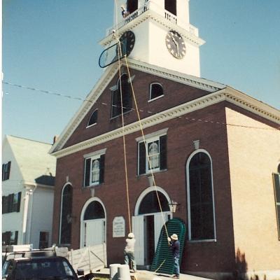 Workers repair a clock tower while others assist from the ground at a historic building.