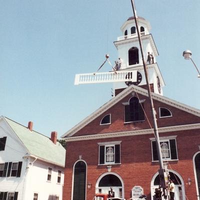 Workers use a crane to install a new railing on a historic building.