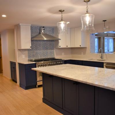 Modern kitchen with white and navy cabinets, marble countertops, and pendant lights.