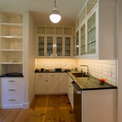 Modern kitchen with white cabinets, black countertops, and glass shelves. Natural light from windows.