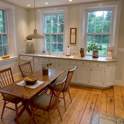 Cozy kitchen with a dining table, wooden floors, and sunlight from large windows.